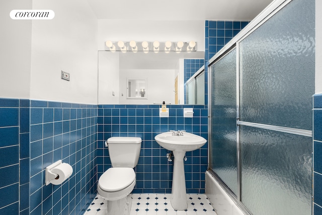 bathroom with tile patterned flooring, bath / shower combo with glass door, a wainscoted wall, toilet, and tile walls