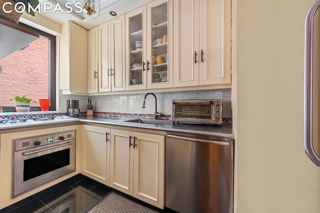 kitchen featuring backsplash, dark tile patterned flooring, sink, stainless steel appliances, and cream cabinetry