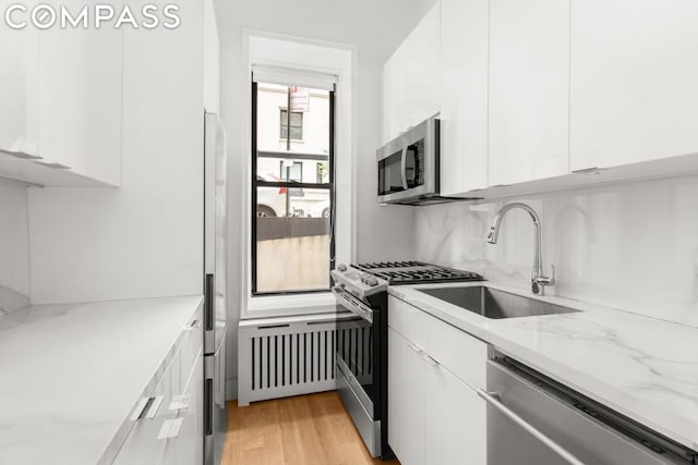 kitchen featuring appliances with stainless steel finishes, white cabinetry, sink, light stone counters, and light wood-type flooring