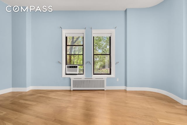 unfurnished room with radiator, light wood-type flooring, cooling unit, and baseboards