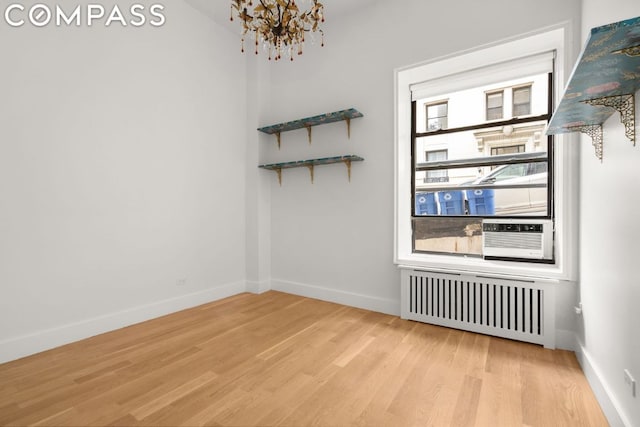 unfurnished room featuring radiator, light hardwood / wood-style floors, and a notable chandelier