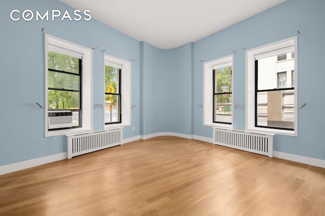 empty room featuring radiator heating unit, light wood-style flooring, and healthy amount of natural light
