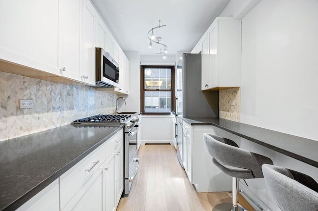 kitchen featuring white cabinetry, stainless steel appliances, tasteful backsplash, light wood-type flooring, and dark stone countertops