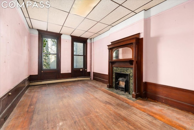 unfurnished living room featuring baseboard heating, a drop ceiling, and hardwood / wood-style floors