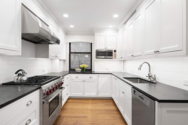 kitchen with appliances with stainless steel finishes, white cabinets, wall chimney range hood, light hardwood / wood-style flooring, and sink