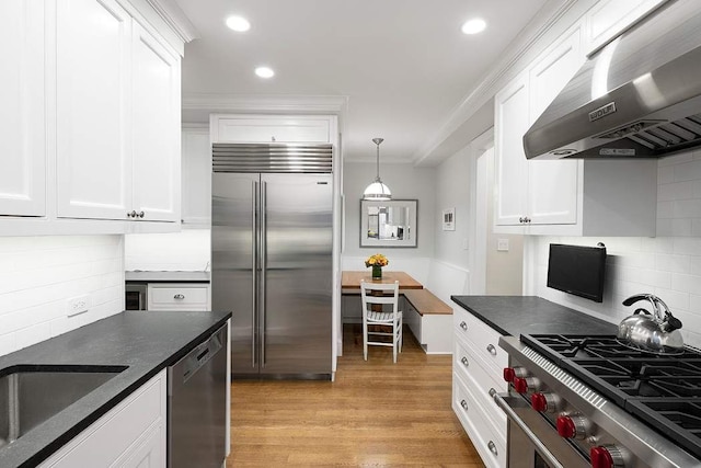 kitchen featuring white cabinets, premium appliances, wall chimney exhaust hood, and light hardwood / wood-style floors