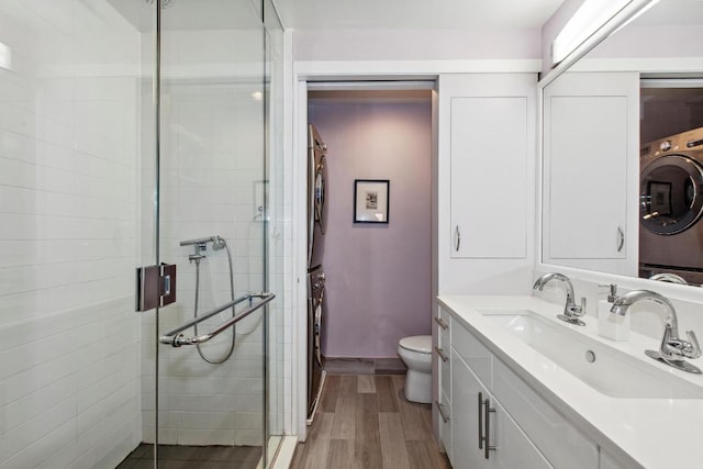 bathroom featuring stacked washer / drying machine, vanity, an enclosed shower, and toilet