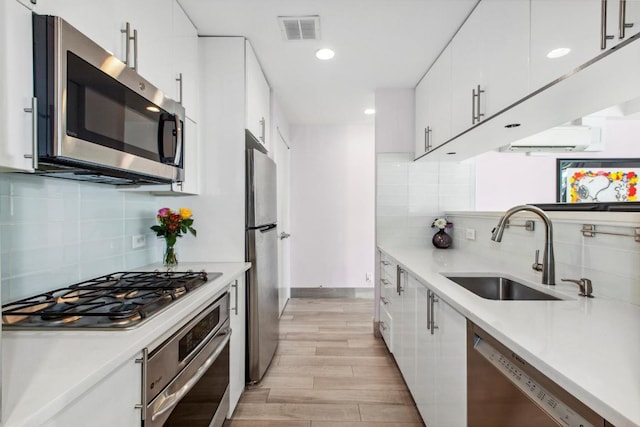 kitchen featuring white cabinetry, stainless steel appliances, tasteful backsplash, light wood-type flooring, and sink