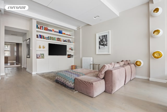 living room with built in shelves, radiator heating unit, and light hardwood / wood-style flooring