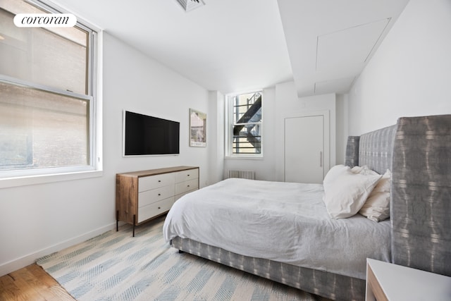 bedroom featuring radiator, light hardwood / wood-style floors, and multiple windows