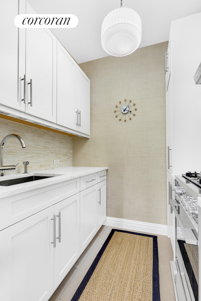 kitchen featuring baseboards, pendant lighting, high end stainless steel range oven, white cabinets, and a sink