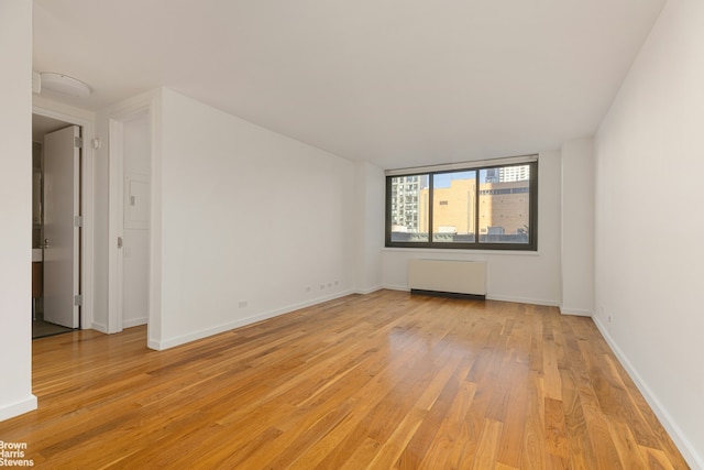 empty room with baseboards, light wood finished floors, and radiator heating unit