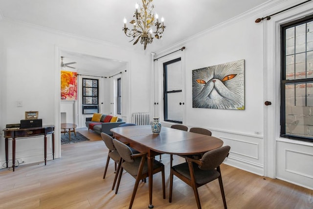 dining area with light wood-type flooring, ornamental molding, and ceiling fan with notable chandelier