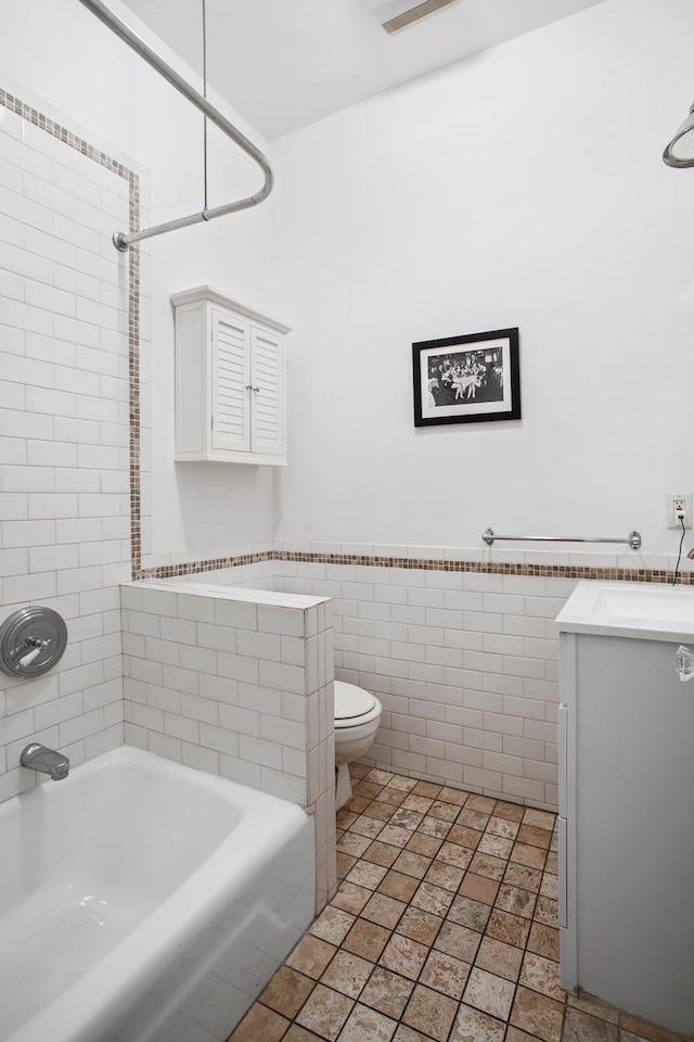 full bath with toilet, shower / bath combination, vanity, tile walls, and wainscoting