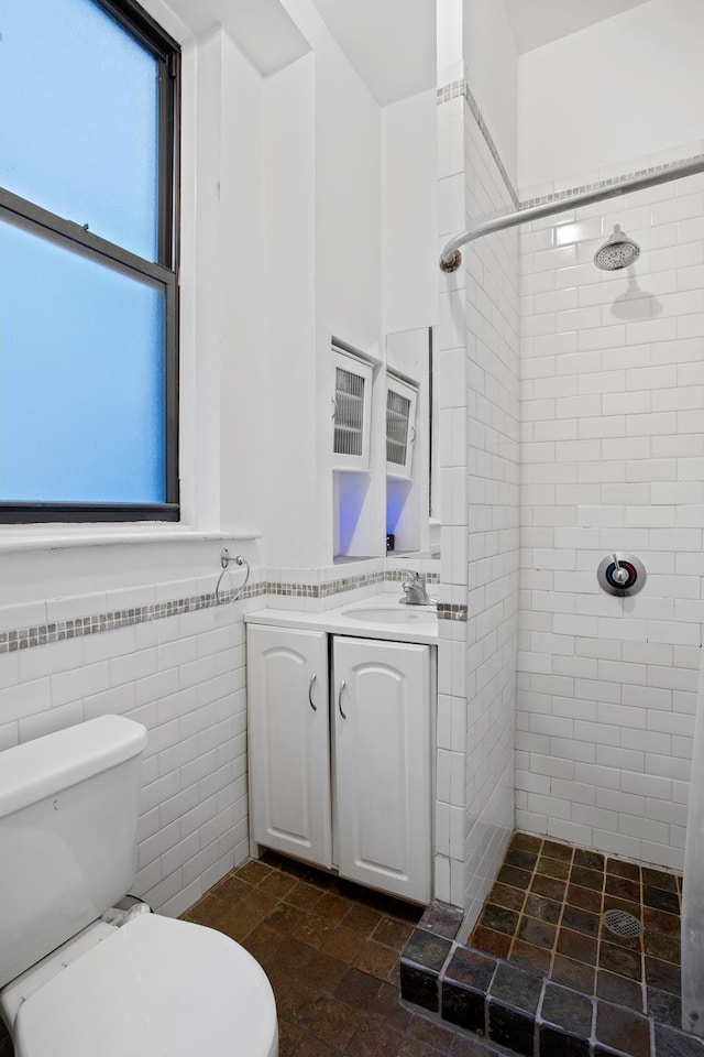 full bath with toilet, a wainscoted wall, vanity, tile walls, and a tile shower