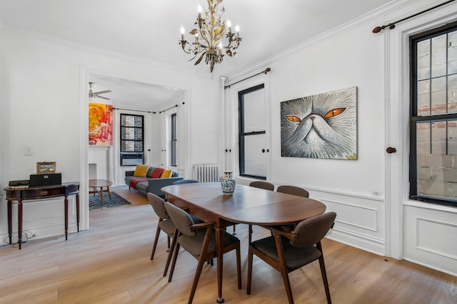 dining area with light wood-type flooring, a wainscoted wall, crown molding, and a decorative wall