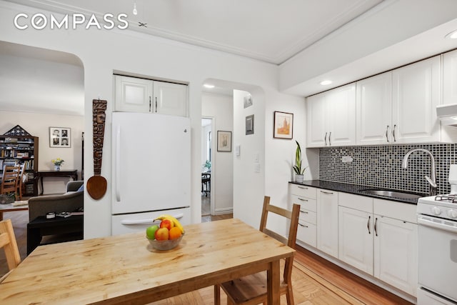 kitchen featuring arched walkways, decorative backsplash, white cabinetry, a sink, and white appliances