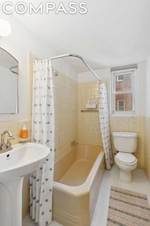 full bathroom featuring toilet, tile walls, tile patterned floors, shower / bathtub combination with curtain, and sink