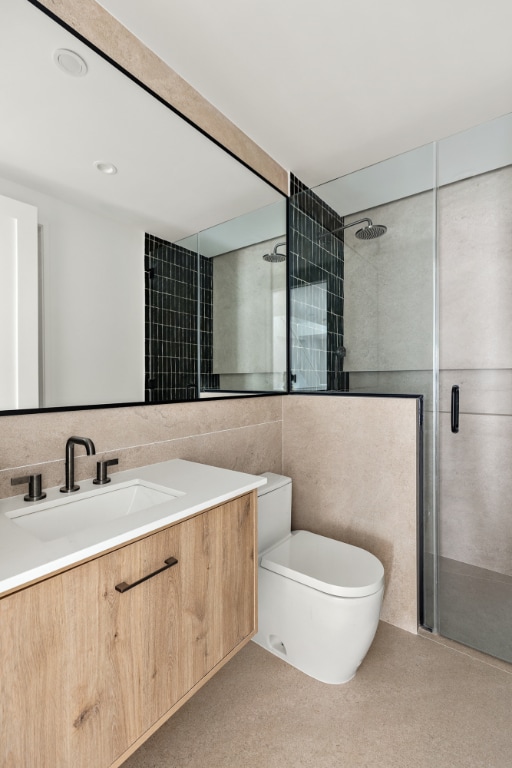 bathroom featuring toilet, vanity, tile walls, decorative backsplash, and a shower with shower door