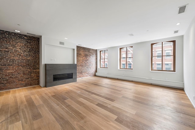 unfurnished living room featuring a glass covered fireplace, visible vents, light wood-type flooring, and brick wall