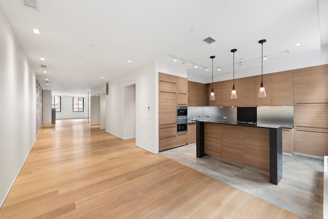 kitchen featuring hanging light fixtures, light hardwood / wood-style flooring, stainless steel oven, and a center island