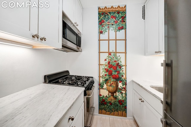 kitchen featuring white cabinets, appliances with stainless steel finishes, light stone counters, and light hardwood / wood-style floors