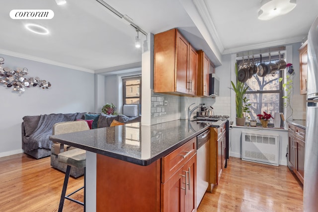 kitchen with radiator, dark stone countertops, a breakfast bar, stainless steel dishwasher, and crown molding