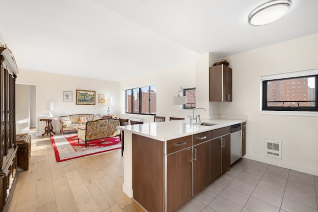 kitchen with dark brown cabinetry, sink, light wood-type flooring, dishwasher, and kitchen peninsula