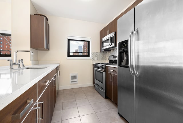 kitchen with sink, decorative backsplash, light tile patterned floors, light stone counters, and stainless steel appliances