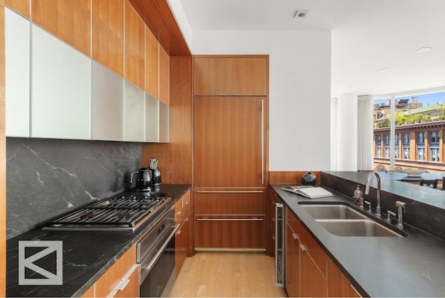 kitchen featuring oven, decorative backsplash, gas cooktop, sink, and light wood-type flooring