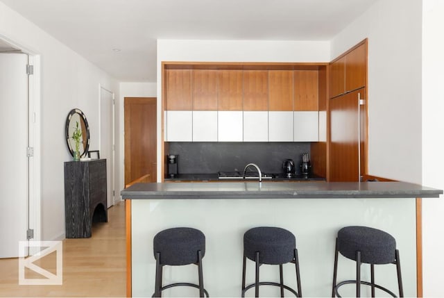 kitchen with kitchen peninsula, decorative backsplash, white cabinets, and light hardwood / wood-style flooring