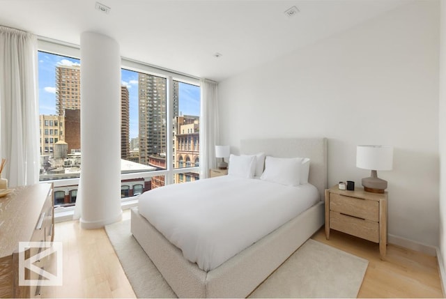 bedroom featuring light wood-type flooring, floor to ceiling windows, and decorative columns