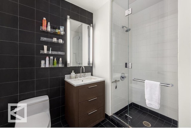 bathroom with toilet, vanity, tile walls, tile patterned floors, and a shower with door