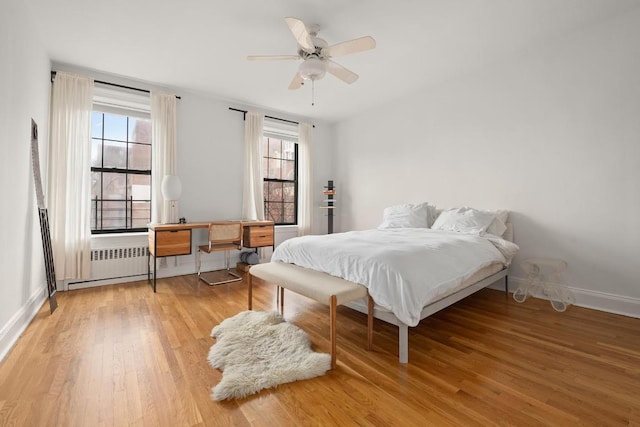 bedroom with hardwood / wood-style flooring, multiple windows, radiator, and ceiling fan