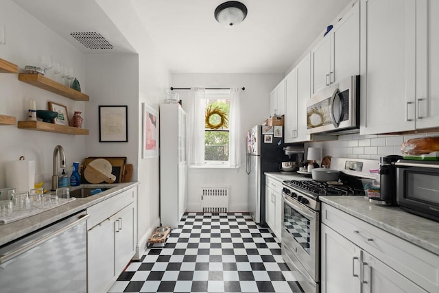 kitchen featuring sink, stainless steel appliances, white cabinets, light stone counters, and radiator heating unit