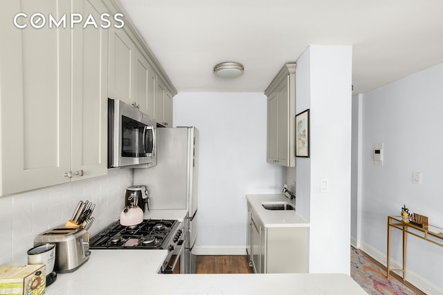 kitchen featuring light countertops, gray cabinetry, decorative backsplash, appliances with stainless steel finishes, and a sink