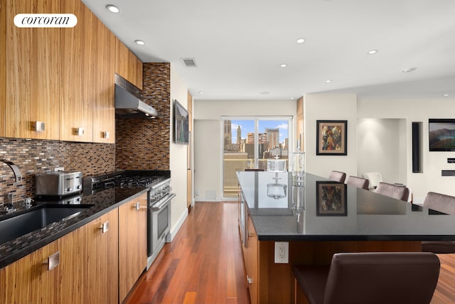 kitchen featuring visible vents, high end stove, tasteful backsplash, a breakfast bar area, and wall chimney range hood