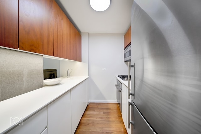 kitchen with light wood-type flooring, modern cabinets, stainless steel appliances, and light countertops