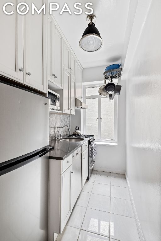 kitchen with decorative backsplash, sink, white cabinetry, appliances with stainless steel finishes, and light tile patterned floors