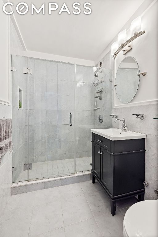 bathroom featuring toilet, tile walls, a shower with shower door, and vanity