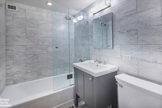 full bathroom featuring toilet, bath / shower combo with glass door, tile walls, and vanity