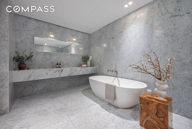 full bathroom featuring a soaking tub, stone wall, marble finish floor, and a marble finish shower