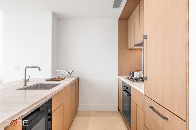 kitchen featuring light brown cabinetry, sink, black oven, and light stone countertops