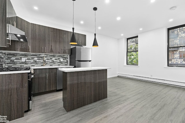 kitchen featuring pendant lighting, appliances with stainless steel finishes, extractor fan, decorative backsplash, and a baseboard radiator