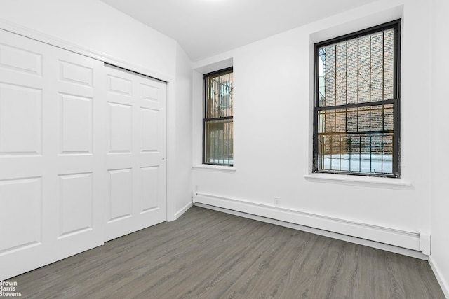 unfurnished bedroom with a closet, multiple windows, baseboard heating, and dark wood-type flooring