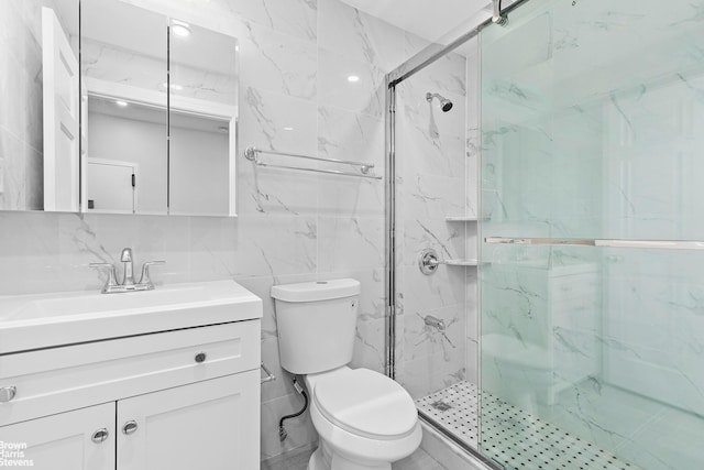 bathroom featuring toilet, vanity, tile walls, a marble finish shower, and decorative backsplash