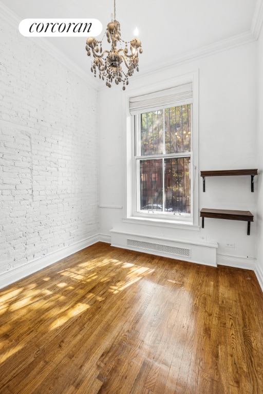 empty room featuring a notable chandelier, brick wall, crown molding, and hardwood / wood-style floors