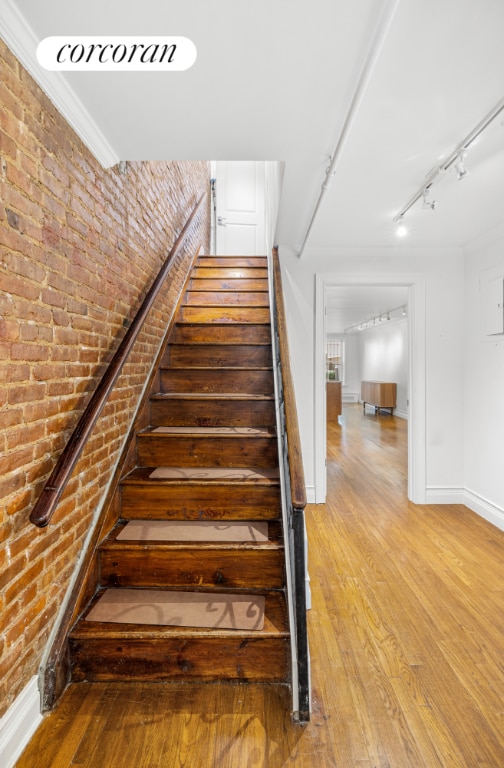 staircase featuring brick wall, ornamental molding, and hardwood / wood-style flooring