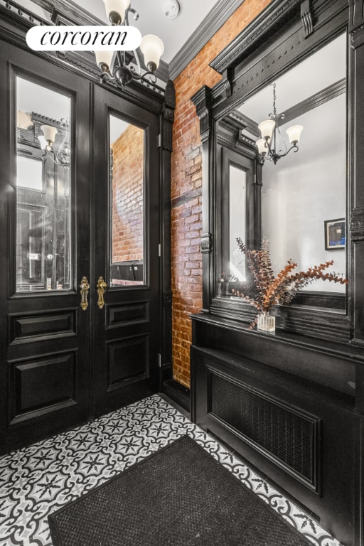 entrance foyer featuring brick wall, ornamental molding, french doors, and an inviting chandelier