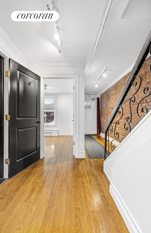 foyer entrance with brick wall, track lighting, wood-type flooring, and crown molding